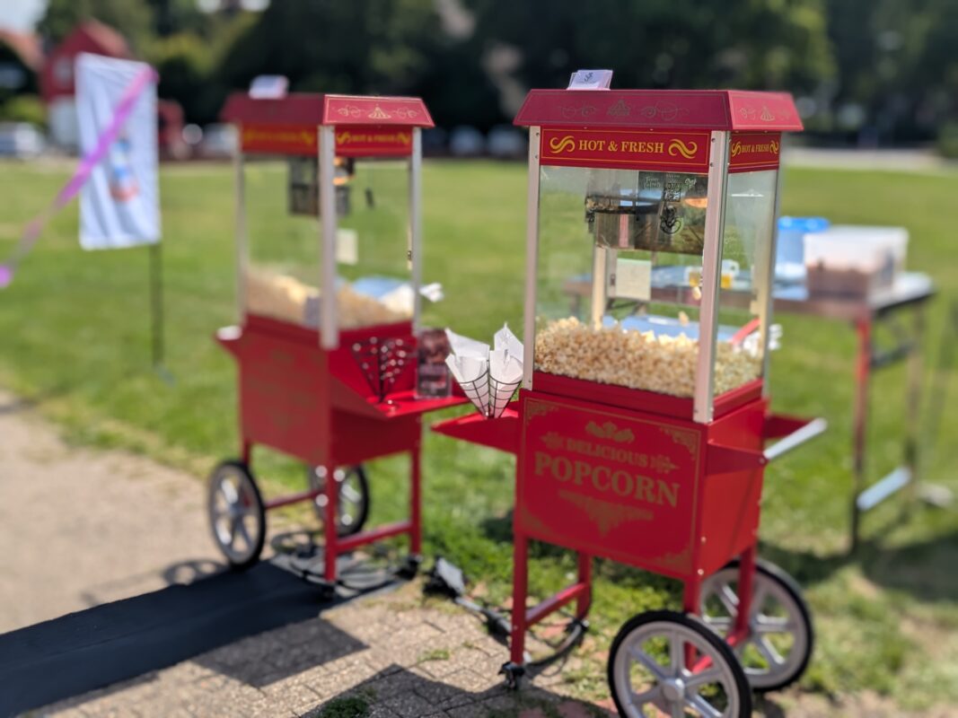 Zwei rote Retro-Popcornmaschinen auf Wagen mit frischem Popcorn bei einem Sommerfest im Freien