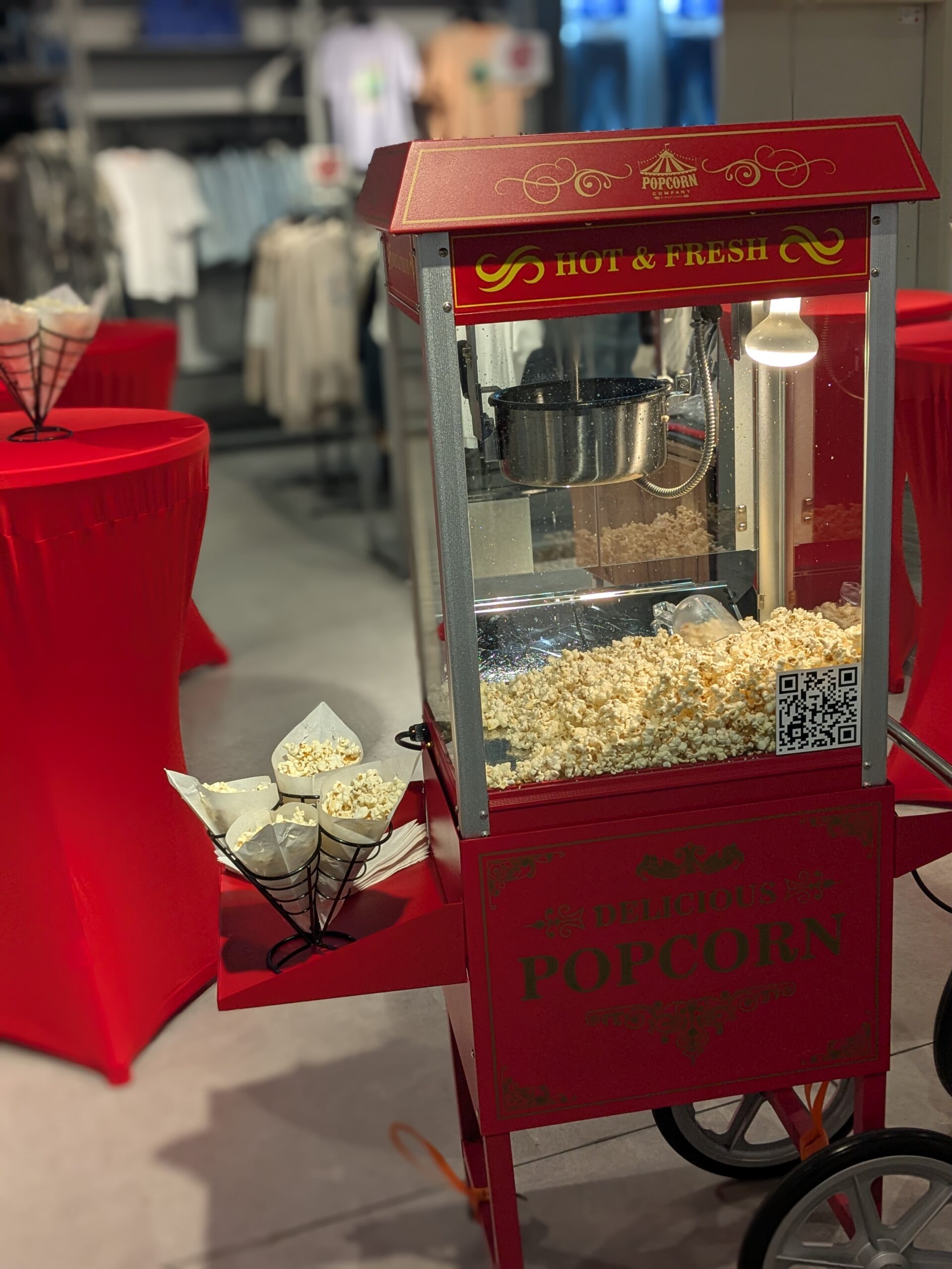 Rote Popcornmaschine mit Spitztüten neben rot eingedeckten Stehtischen bei einem Firmen- und Promotion-Event