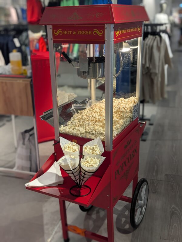 Rote Retro-Popcornmaschine auf Wagen, frisches Popcorn im Glaskasten, davor Spitztüten im Ständer