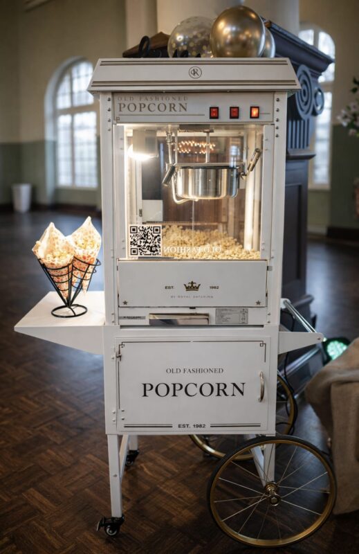 Weiß-Gold-Popcornmaschine im Retro-Stil auf Wagen mit Speichenrädern, daneben Popcorn in Spitztüten